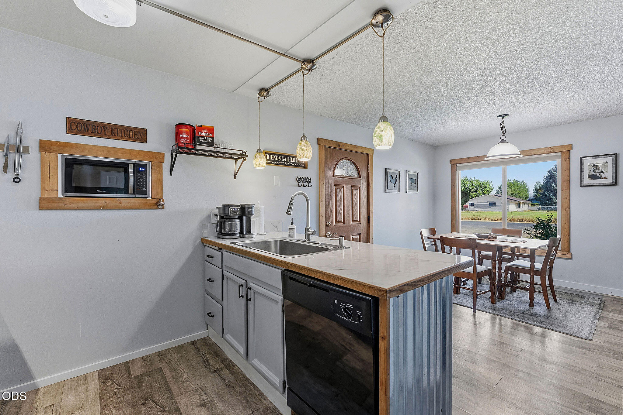 Kitchen with a long island and sink opening onto a dining area beside a large window.