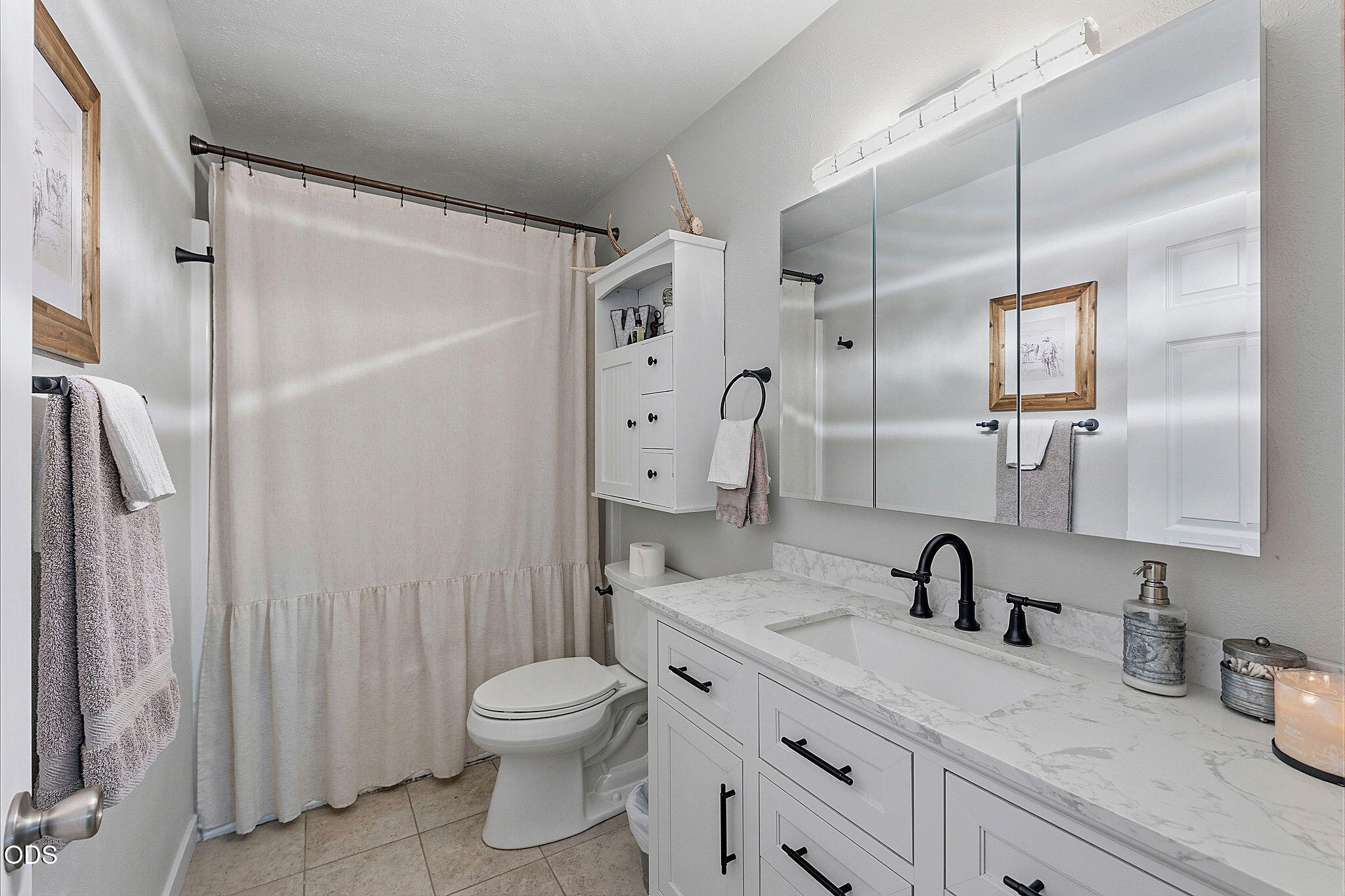 Bathroom with a long white vanity, marble-look counter, black fixtures, and mirrored cabinets.