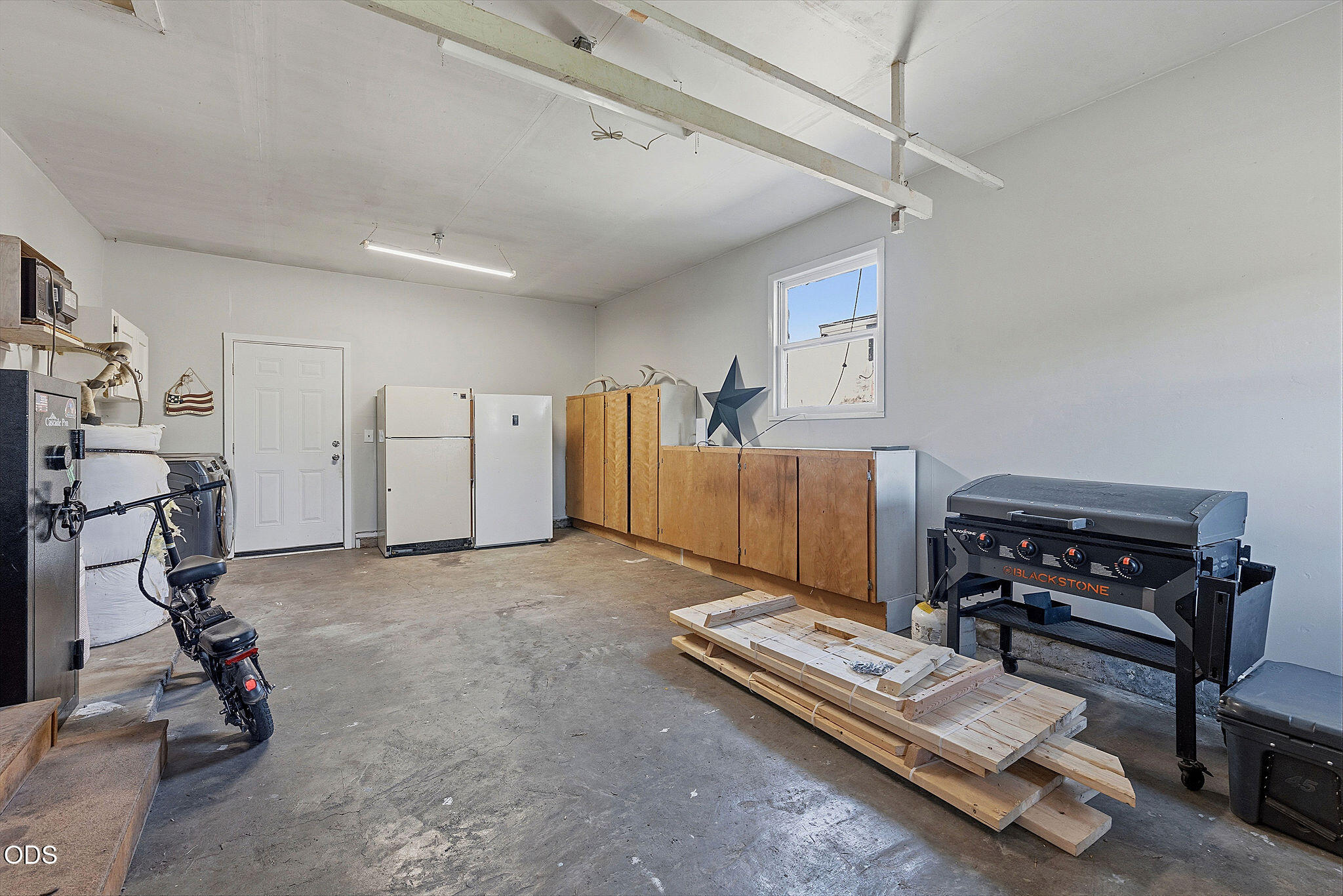 Garage with wooden cabinets, two refrigerators, a motorcycle, and a Blackstone griddle.