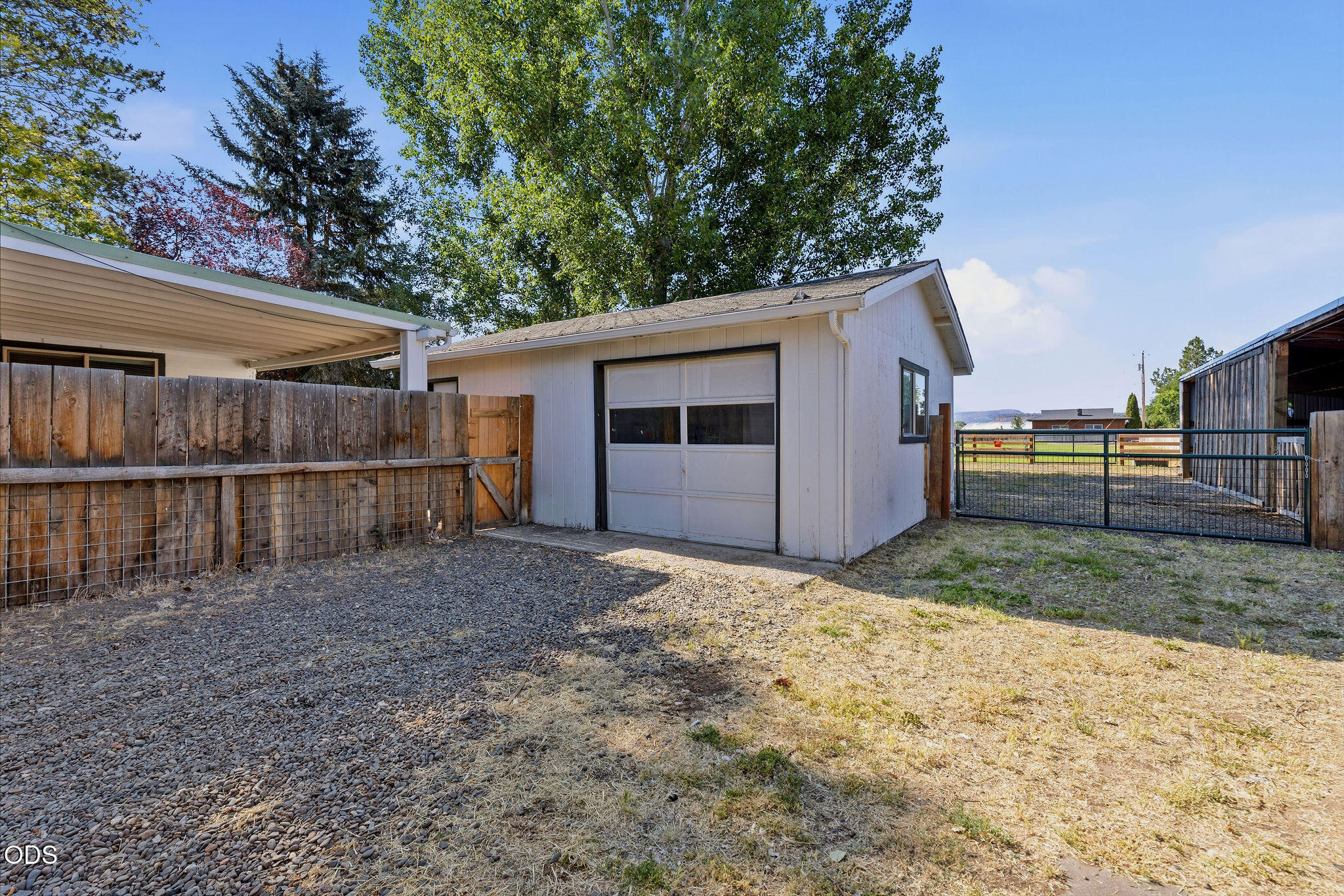 Detached white garage beside a fenced gravel yard and metal gate.