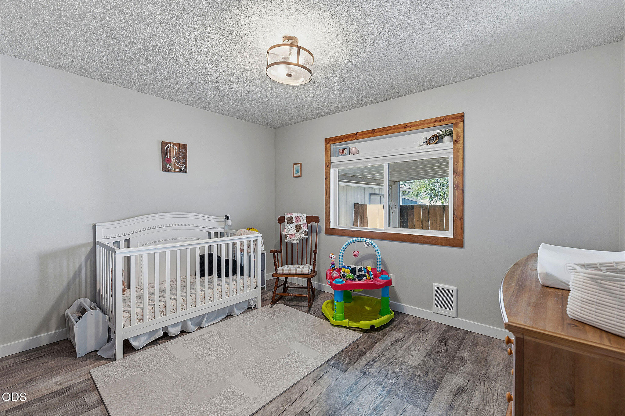Nursery with a white crib, rocking chair, colorful activity center, and wood-trimmed window.