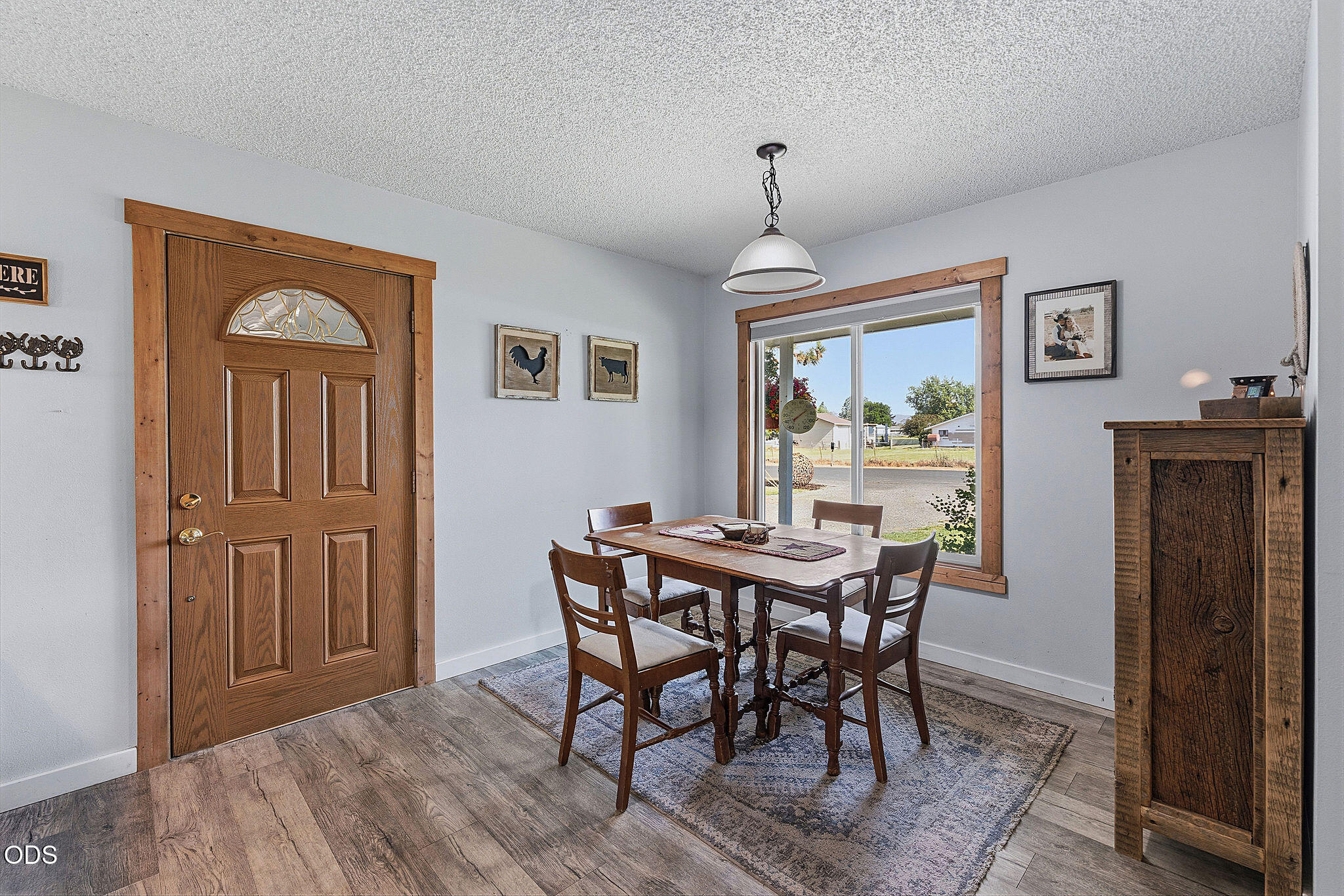 Dining area with a wooden entry door, table and chairs, and a large window overlooking the yard.