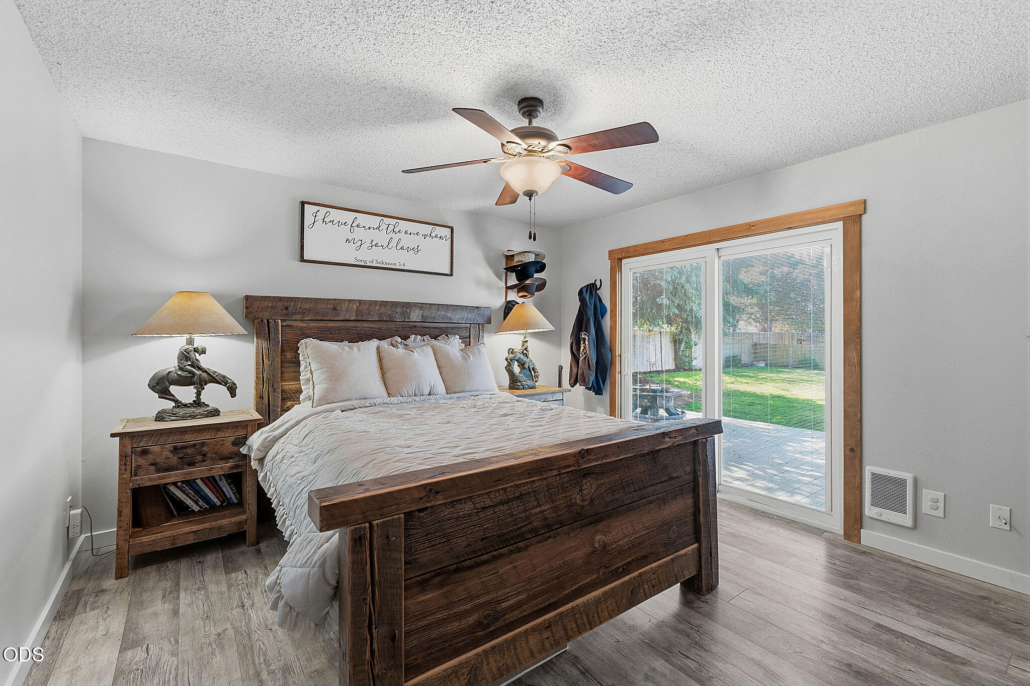 Rustic wood bed with white bedding beside a sliding glass door opening to a green yard.