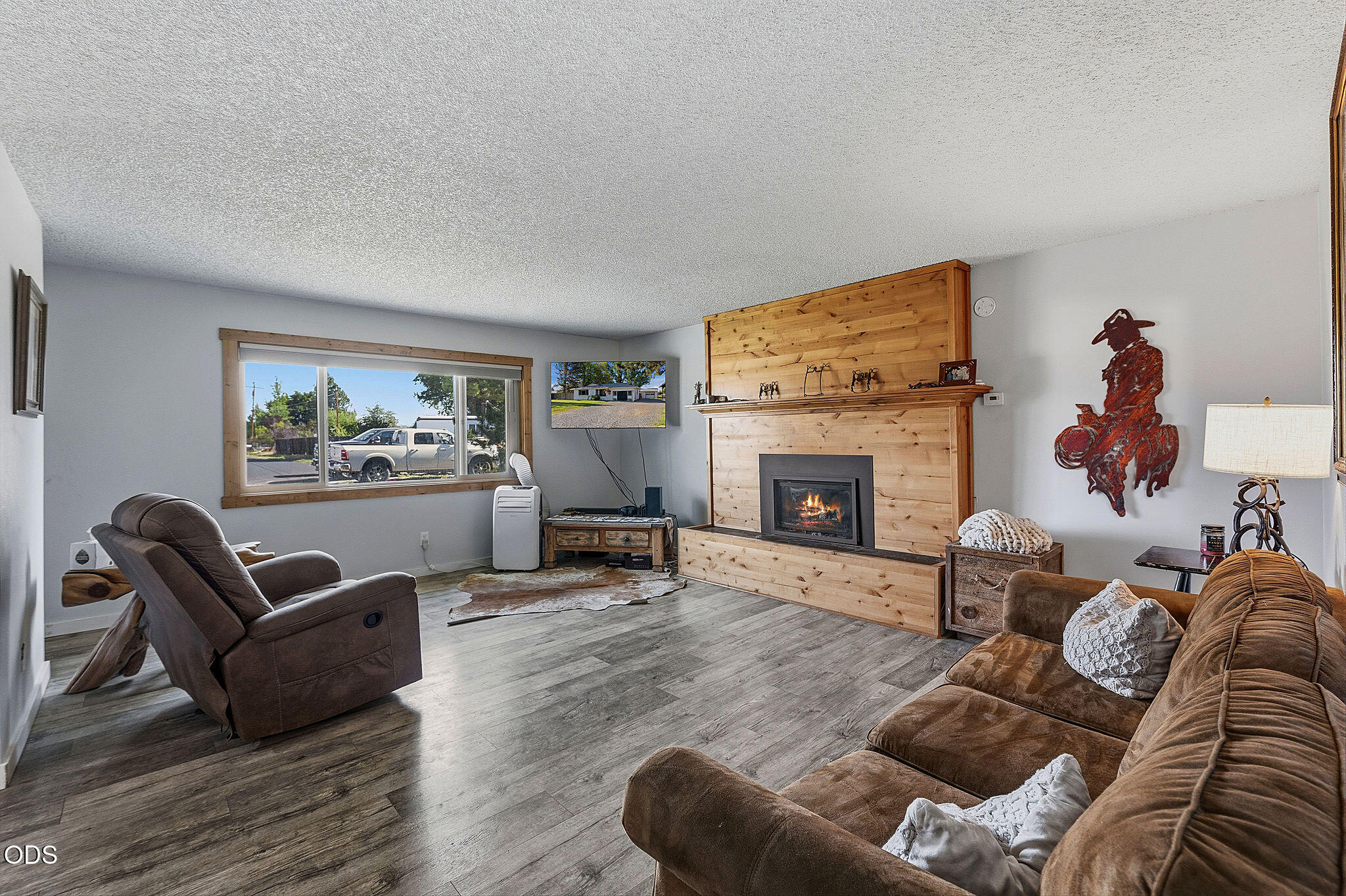 Living room with a wood-paneled fireplace, brown sofas, and gray plank flooring.