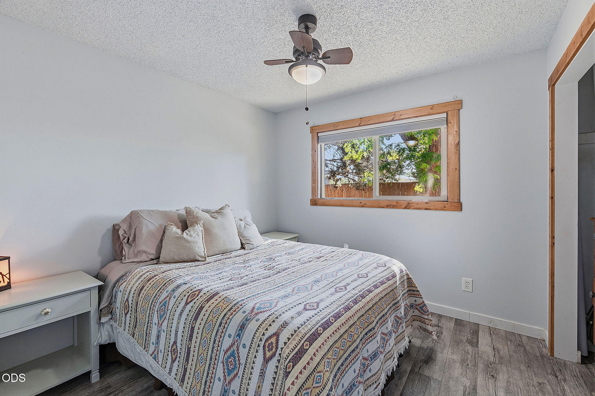 Furnished bedroom with a patterned quilt, ceiling fan, and wood-trimmed window.