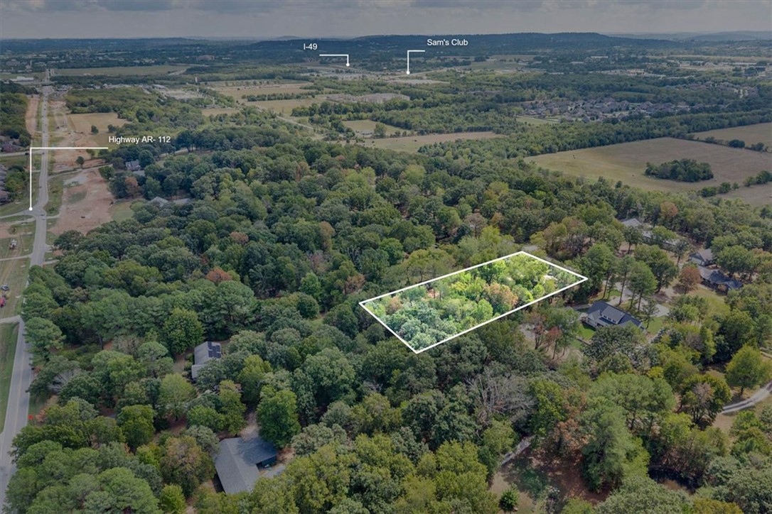 Aerial view of a wooded parcel outlined among homes and fields near Highway AR-112.