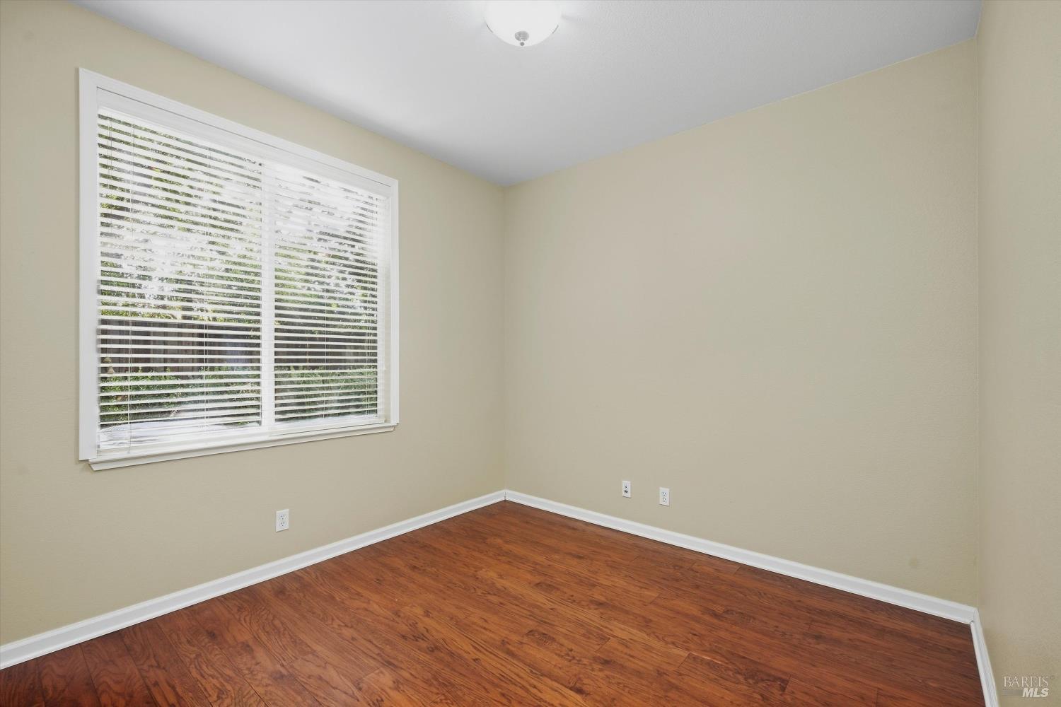 Empty room with reddish wood-look flooring and a large window with white blinds.