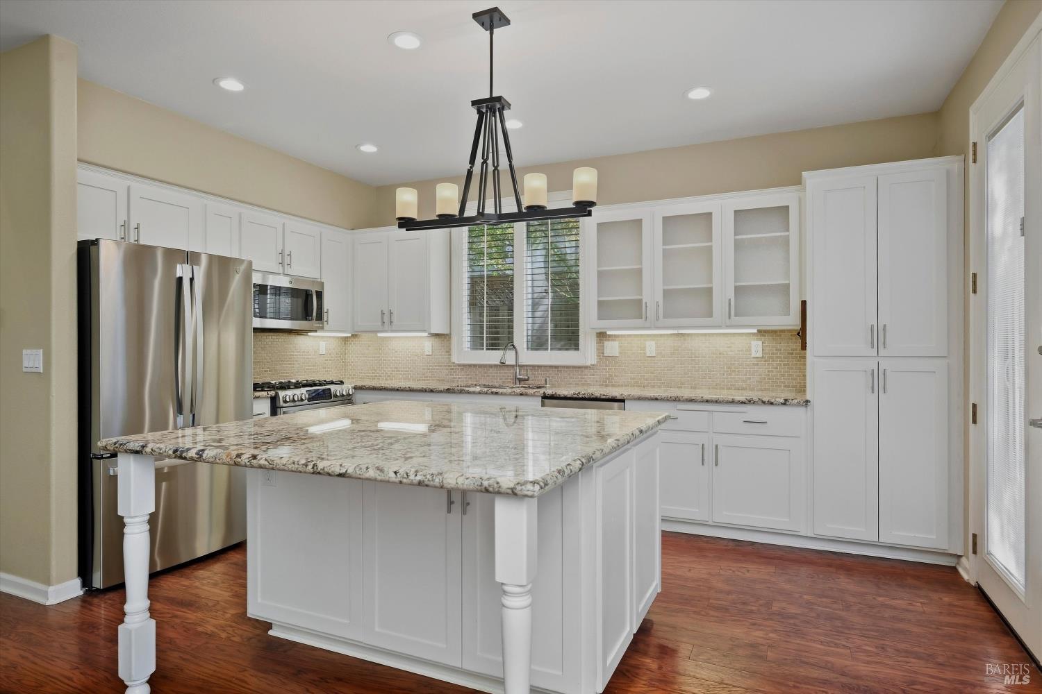 Kitchen with white cabinets, stainless steel appliances, and a large granite-topped island.