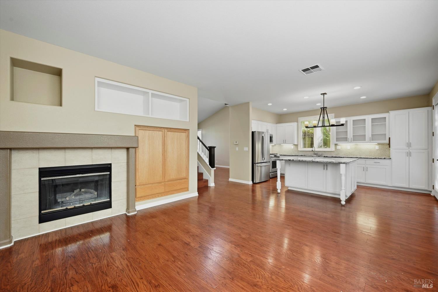 Open kitchen and living area with a white island, stainless appliances, and tiled fireplace.