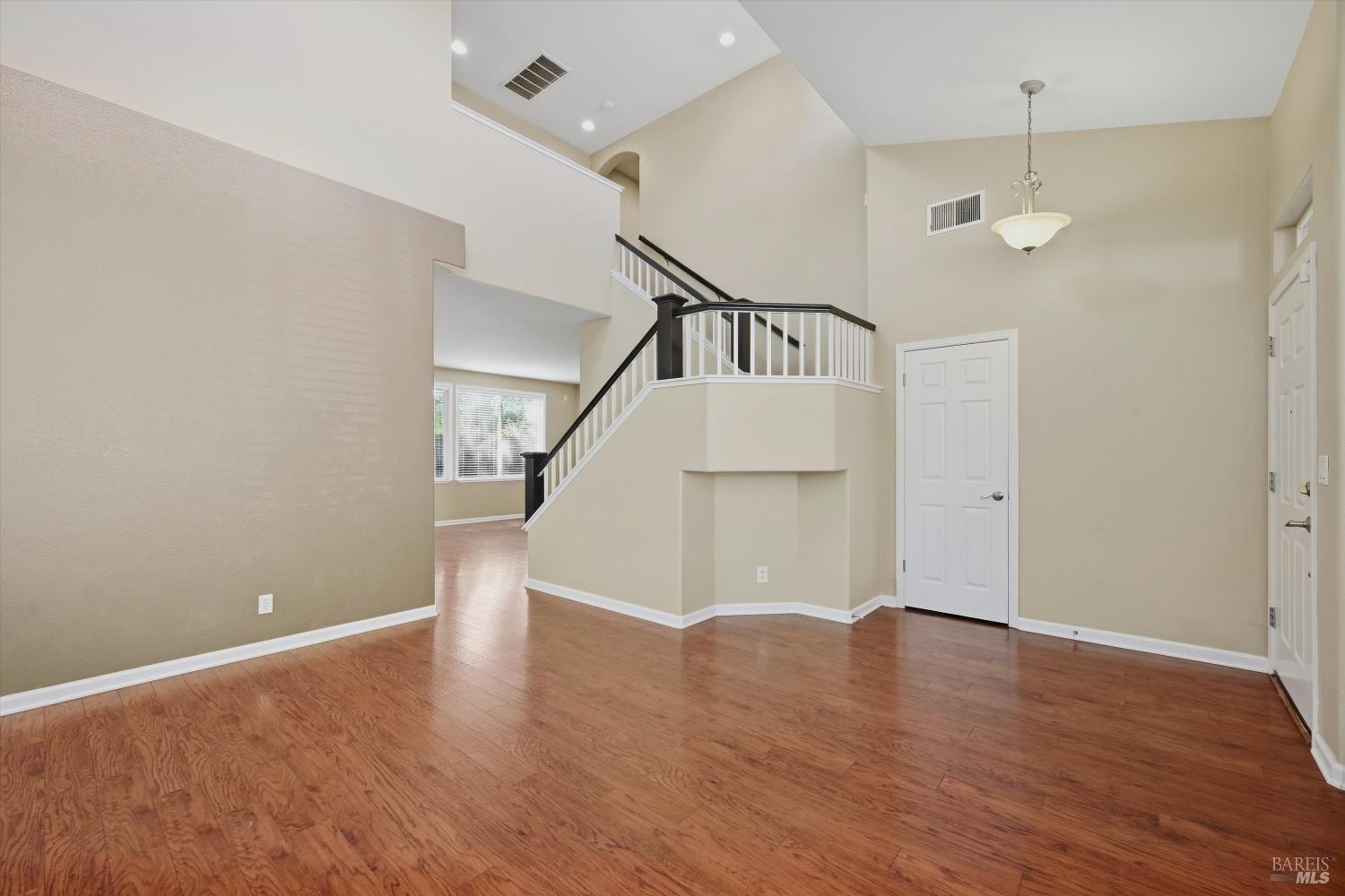 Empty foyer with hardwood floors, high ceilings, and a staircase with dark handrails.