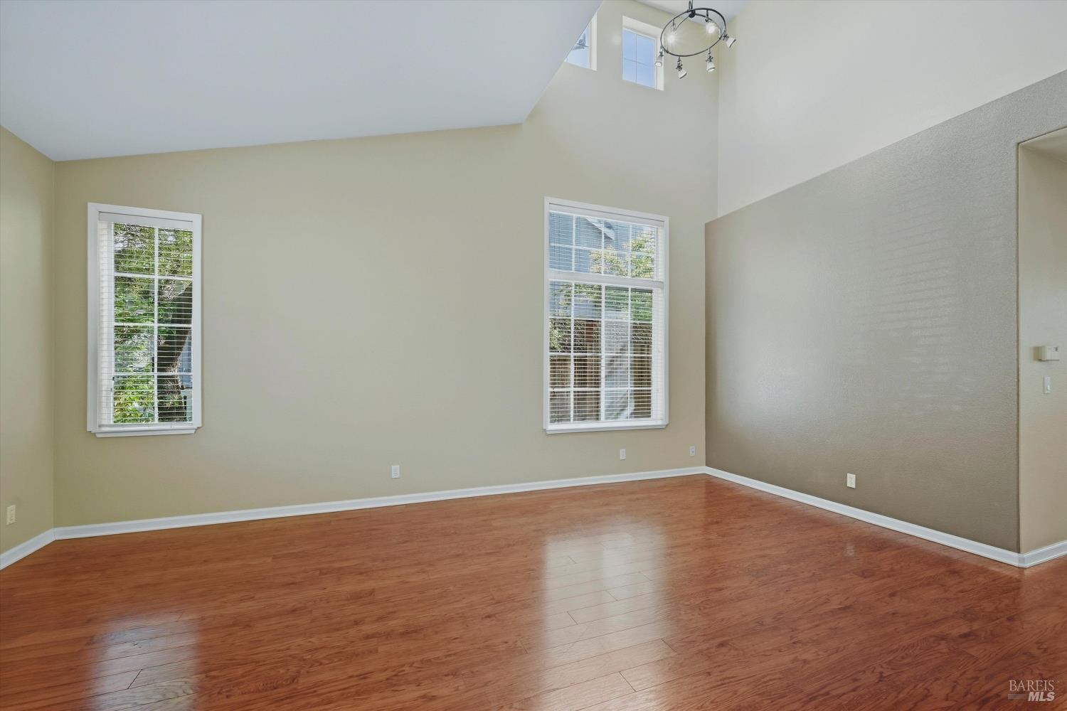 Vacant room with hardwood floors, tall windows, and a vaulted ceiling.