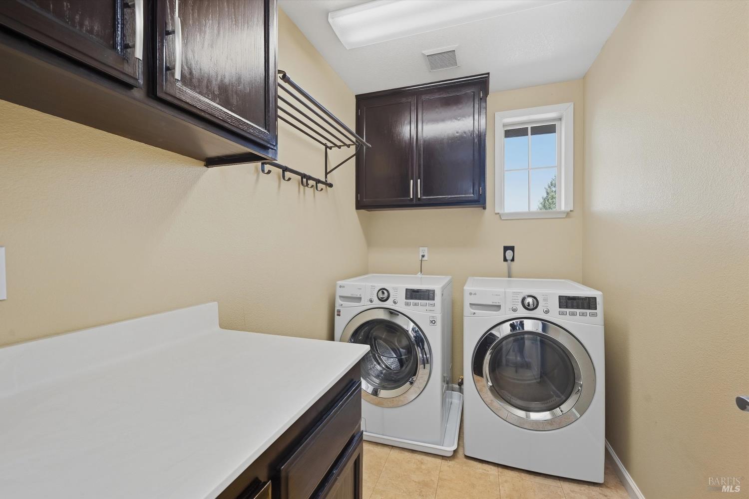 Laundry room with front-loading washer and dryer beneath dark cabinets, beside a white folding counter.