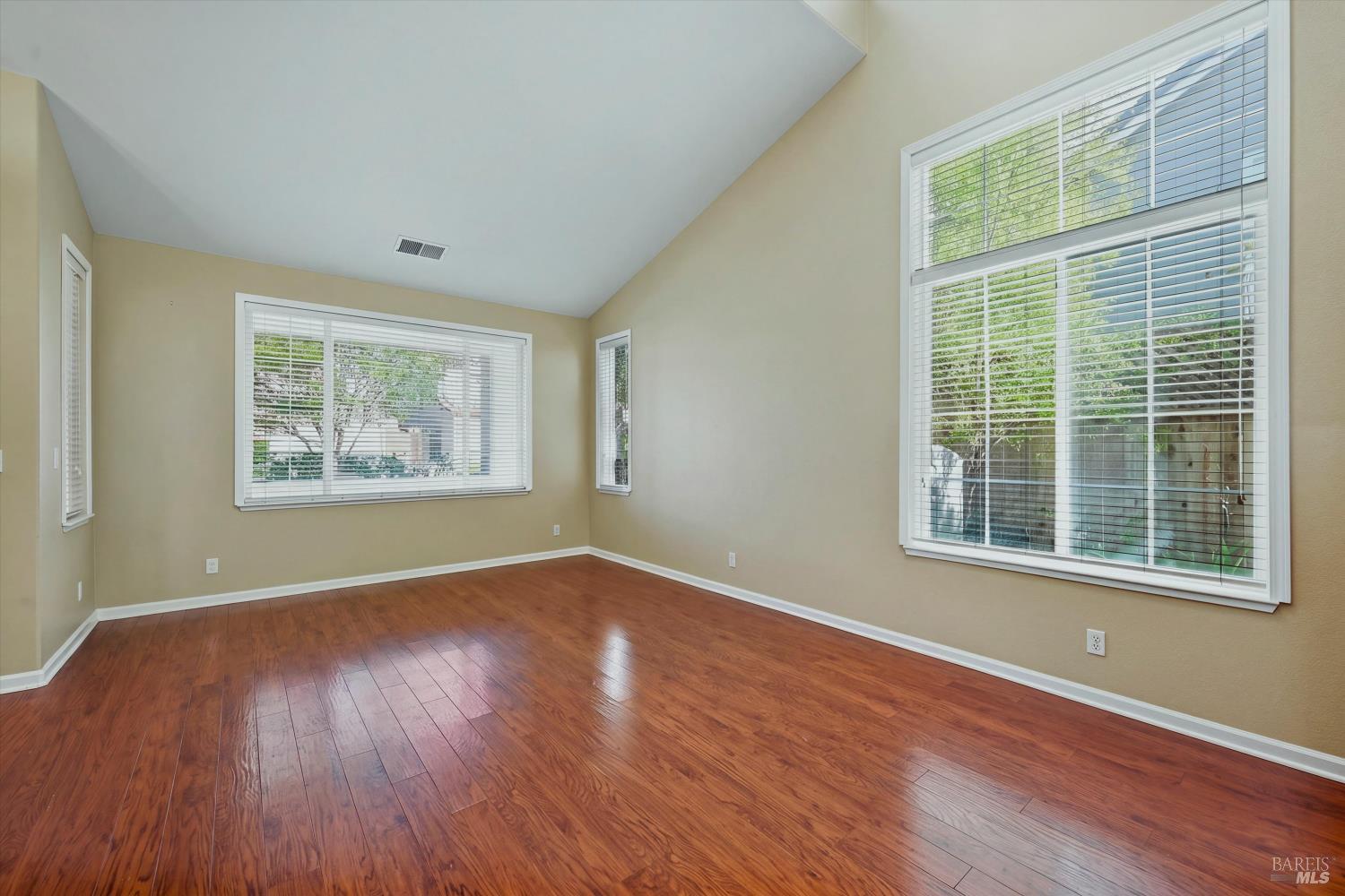 Empty room with hardwood floors, a vaulted ceiling, and large windows with blinds.