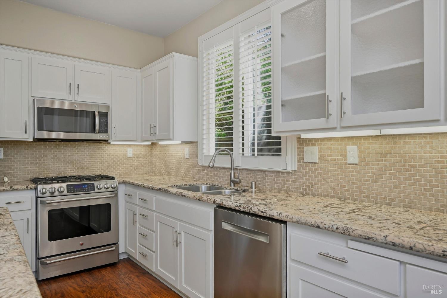 Kitchen with white cabinets, granite counters, stainless steel appliances, and plantation shutters.