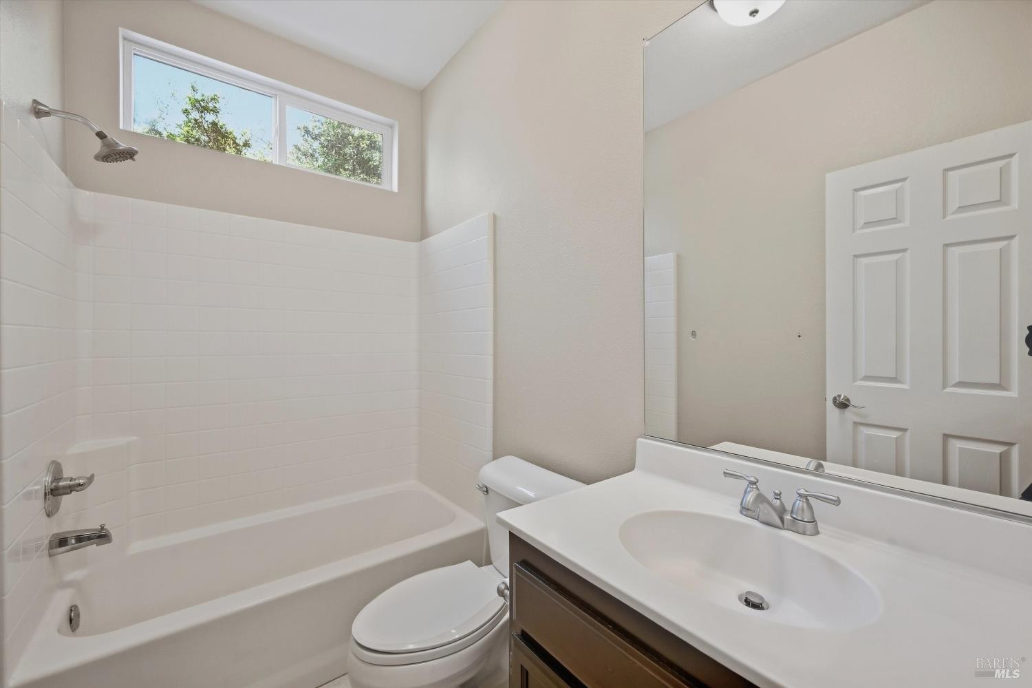 Bathroom with a white tiled tub and shower, high windows, and a dark wood vanity.