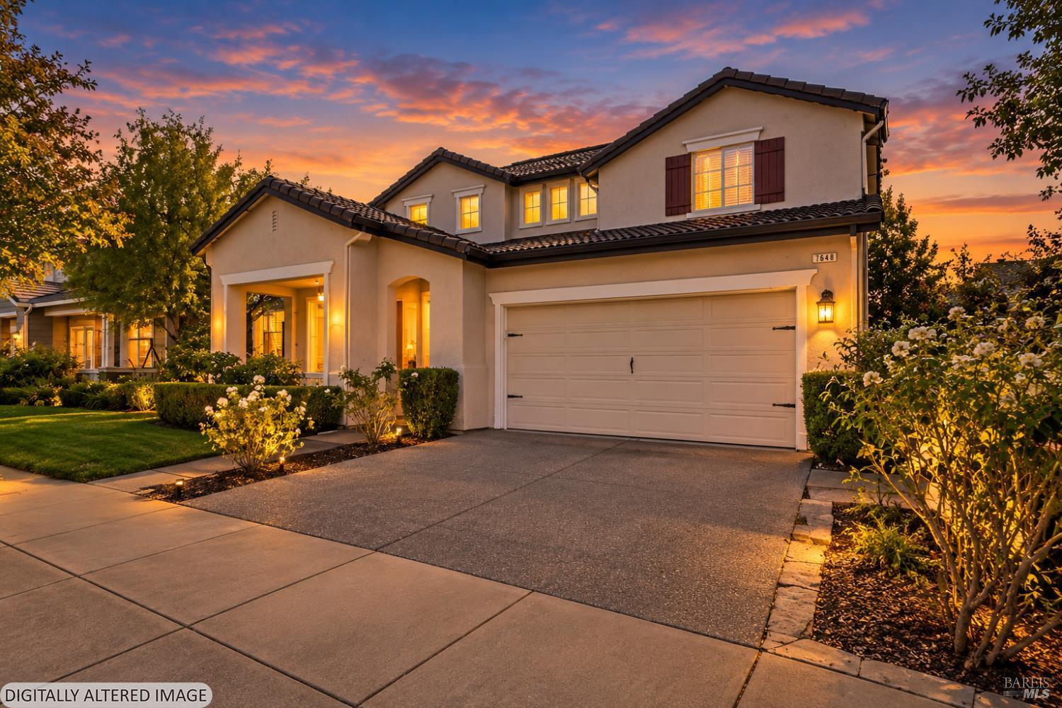 Two-story home with a double garage and landscaped yard, photographed at dusk beneath a colorful sunset sky.