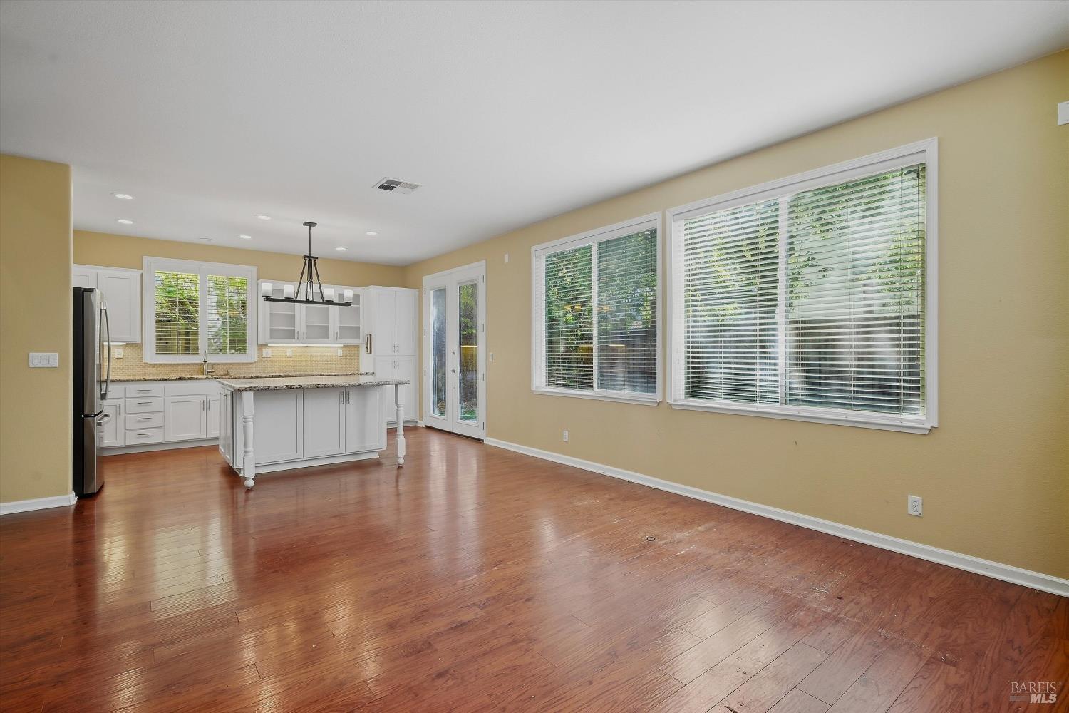 Open-plan kitchen and living area with a white island, wood floors, and large windows.