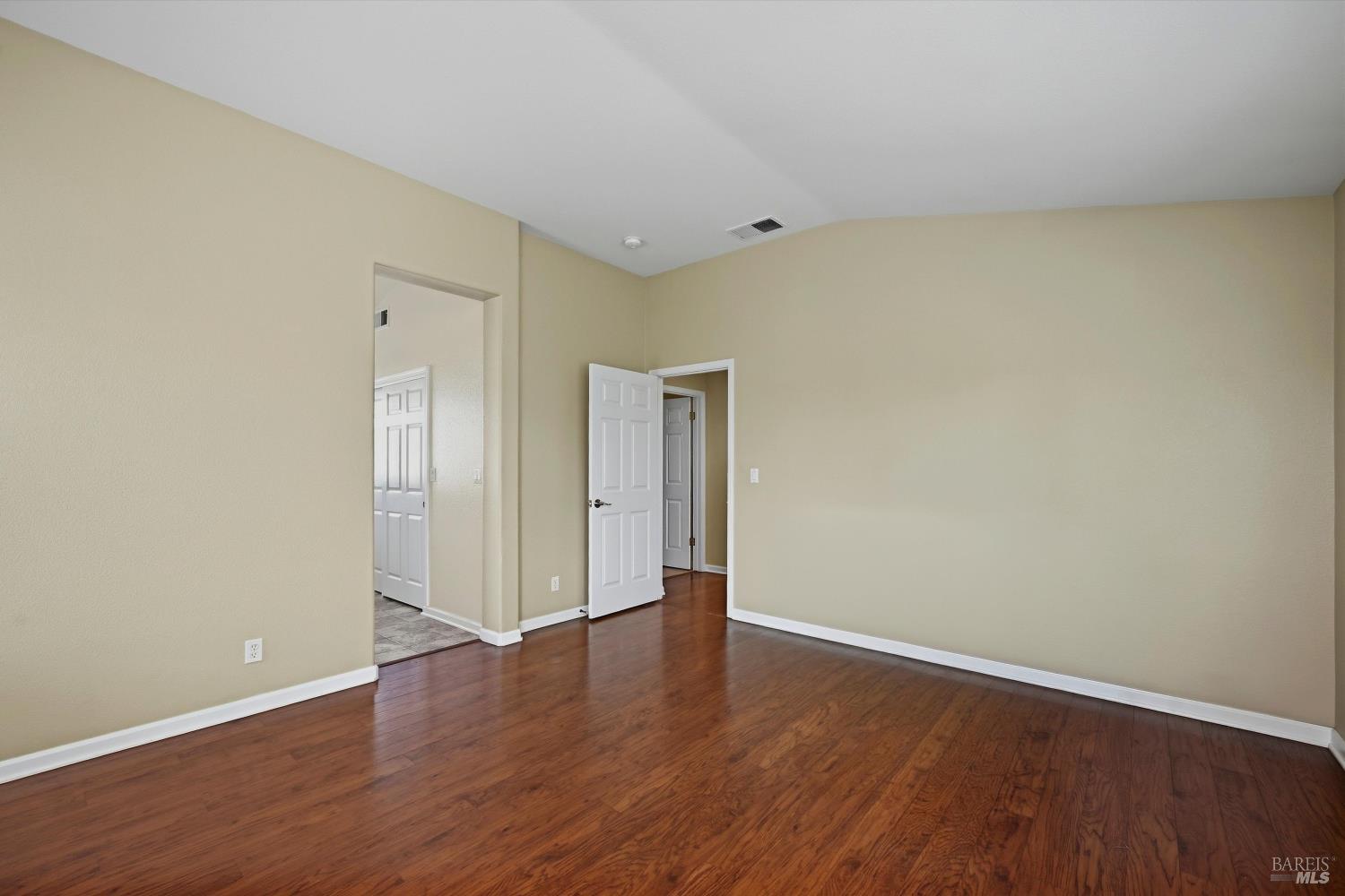 Empty bedroom with reddish-brown hardwood floors and two open doorways.