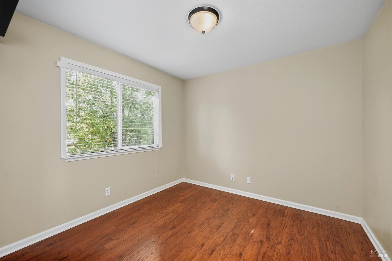 Empty room with warm wood flooring and a wide window with white blinds.