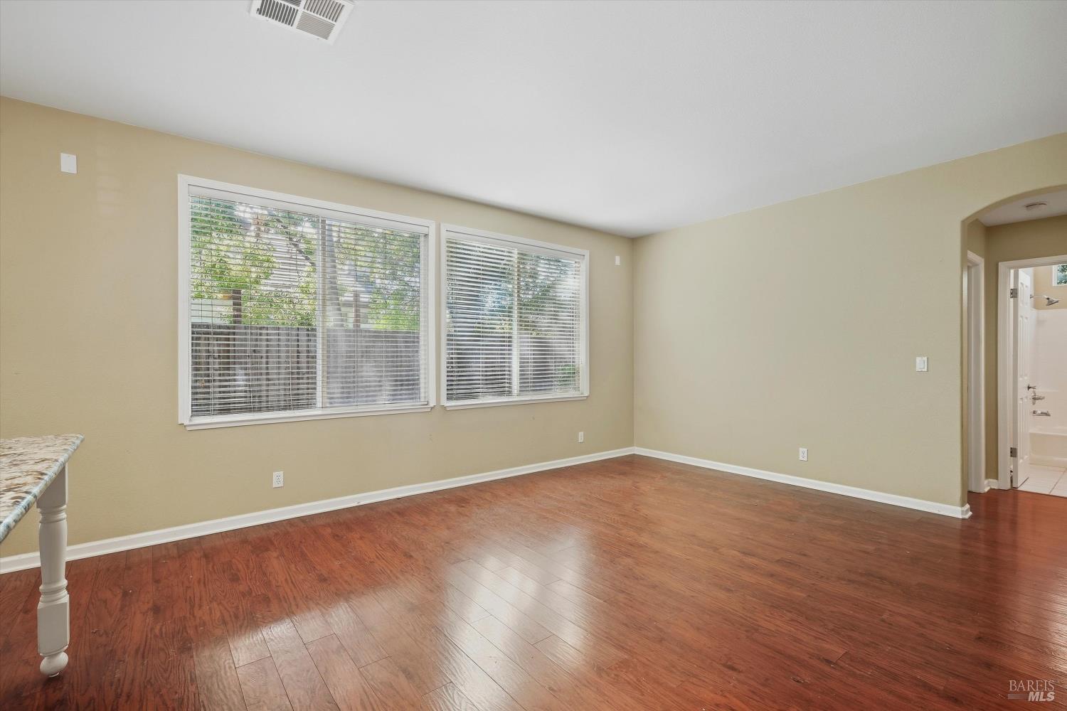 Vacant room with hardwood floors, wide windows, and an arched bathroom doorway.