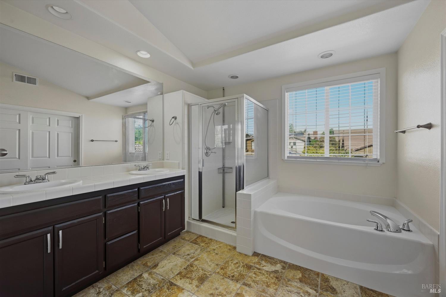 Bathroom with a corner soaking tub, glass shower, and dark wood double vanity.