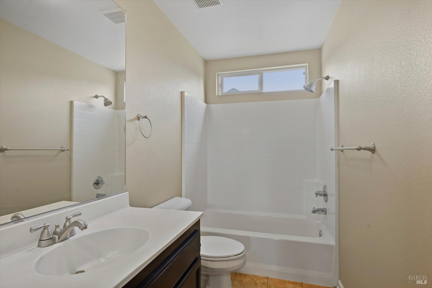 Bathroom with a white tub and tiled surround, single-sink vanity, and high horizontal window.