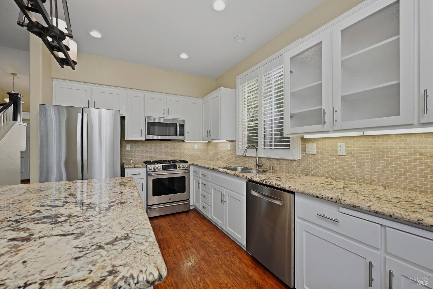 Kitchen with white cabinets, granite counters, stainless steel appliances, and hardwood floors.
