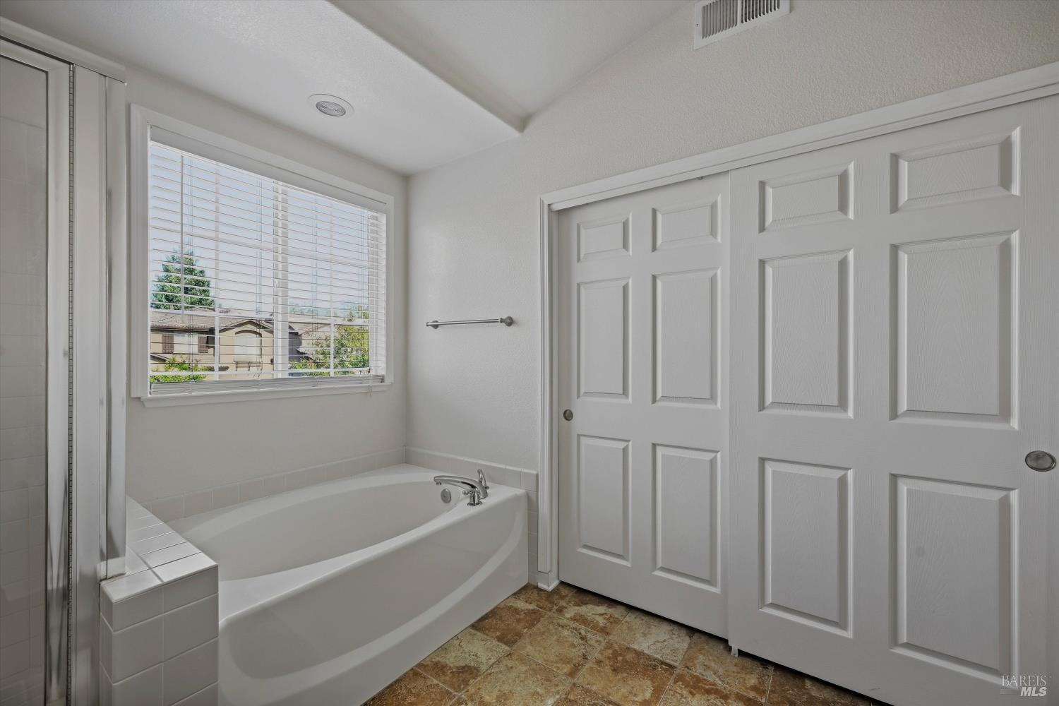 Bathroom with a built-in bathtub beneath a window with blinds and large white paneled sliding doors.