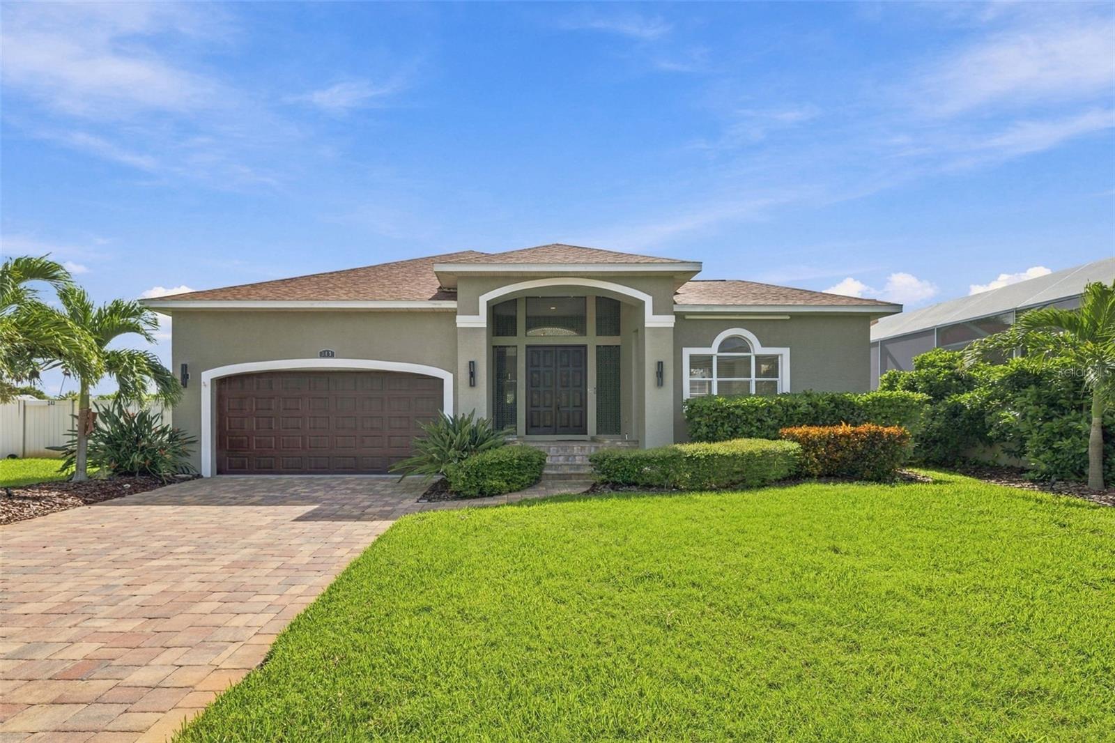 Single-story home with a two-car garage, arched entry, paver driveway, and landscaped lawn.