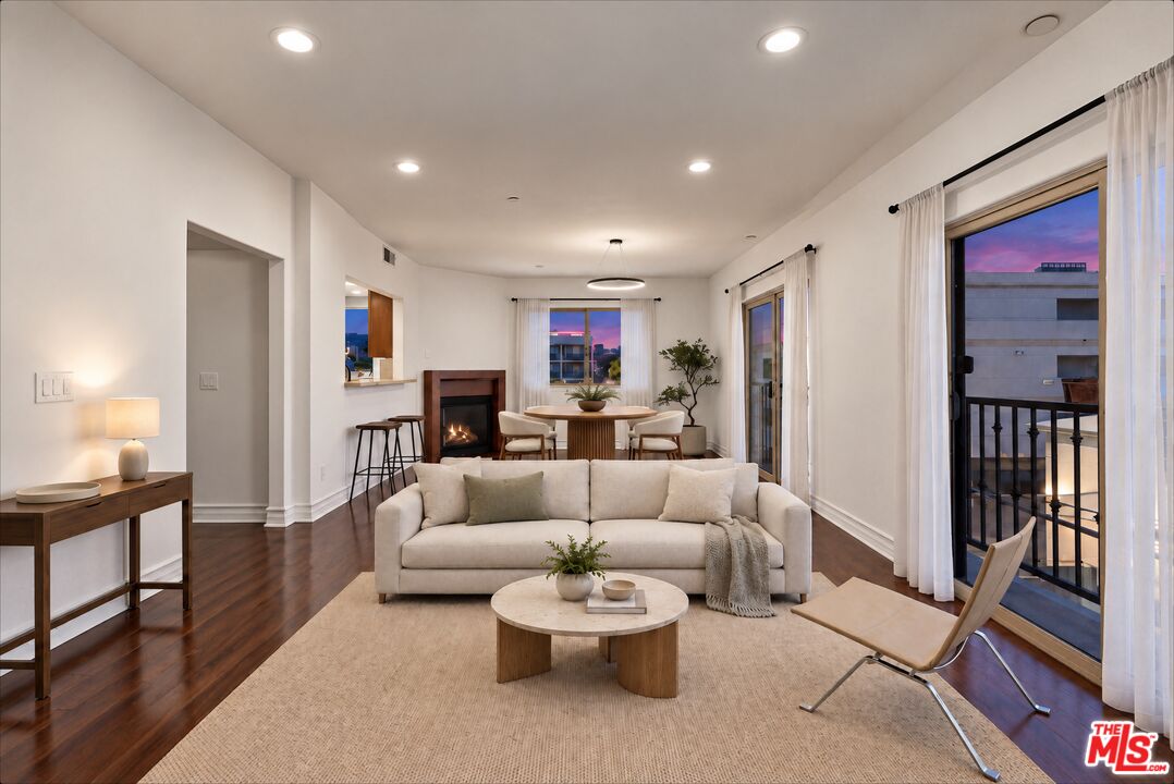 Staged living room with a white sofa, fireplace, and large windows showing a dusk city view.
