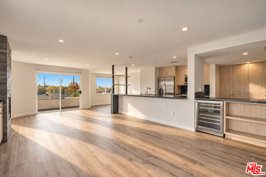 Open-plan living area and modern kitchen with light wood cabinets, island, and balcony doors.
