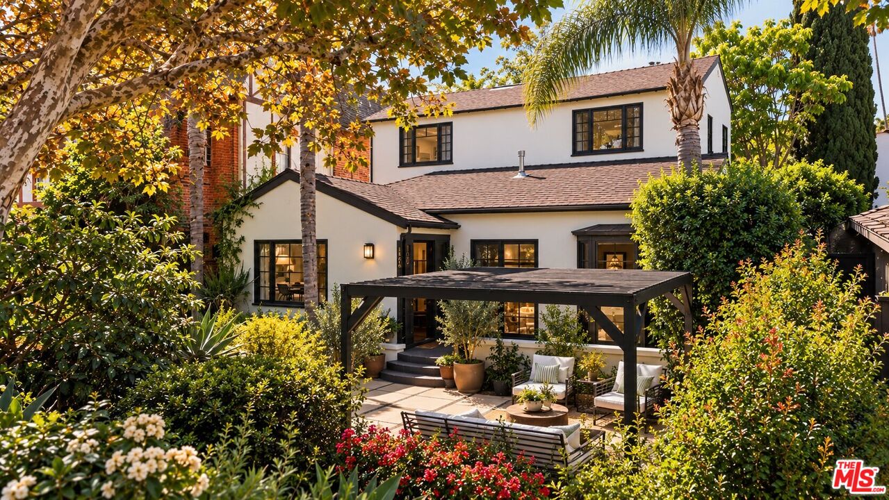 Two-story white house behind a landscaped patio with a pergola and outdoor seating.