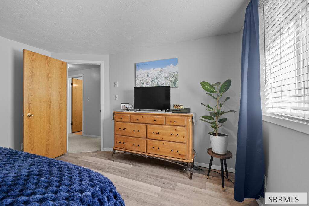 Bedroom with a blue bedspread, wooden dresser, television, and window with blue curtains.