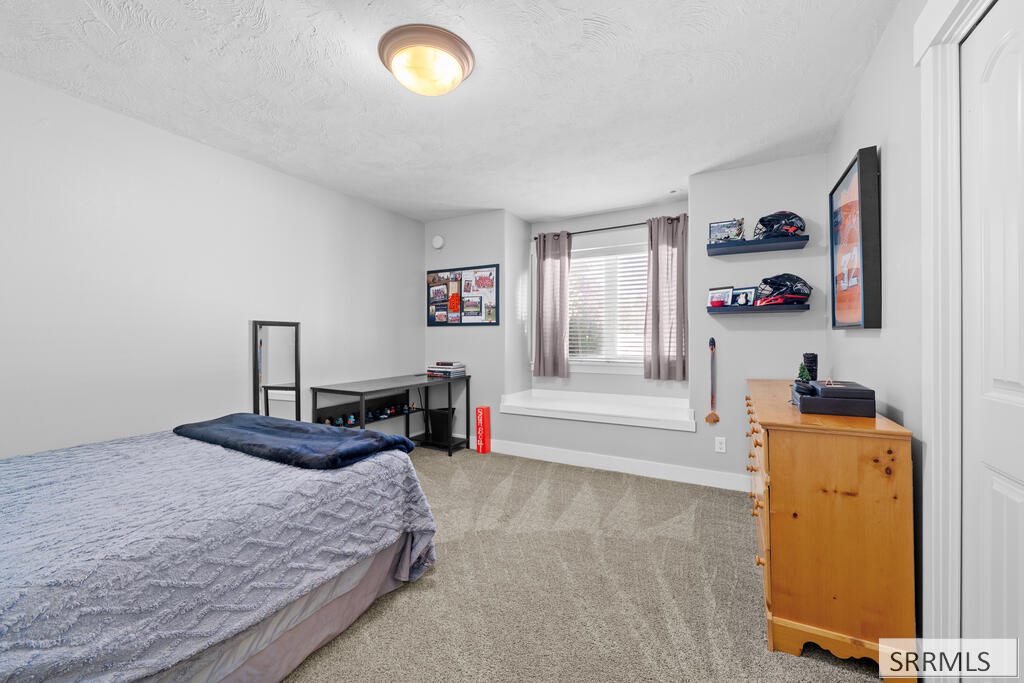 Bedroom with a gray-quilted bed, mauve curtains, and sports memorabilia on wall shelves.