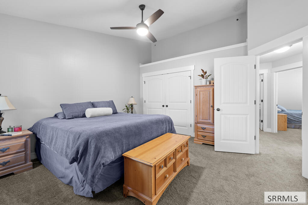 Furnished bedroom with blue-gray bedding, wooden chests, and an open doorway to another bedroom.