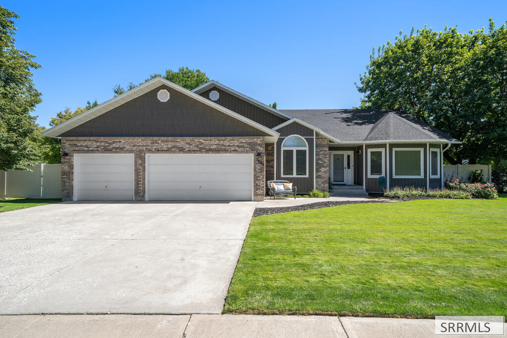 Single-story brick home with two white garage doors, a wide driveway, and a neatly mowed lawn.