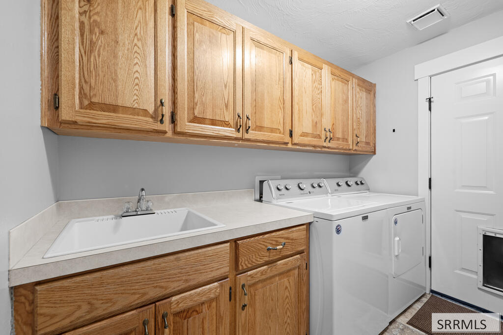 Laundry room with a utility sink, wood cabinetry, and white washer and dryer.