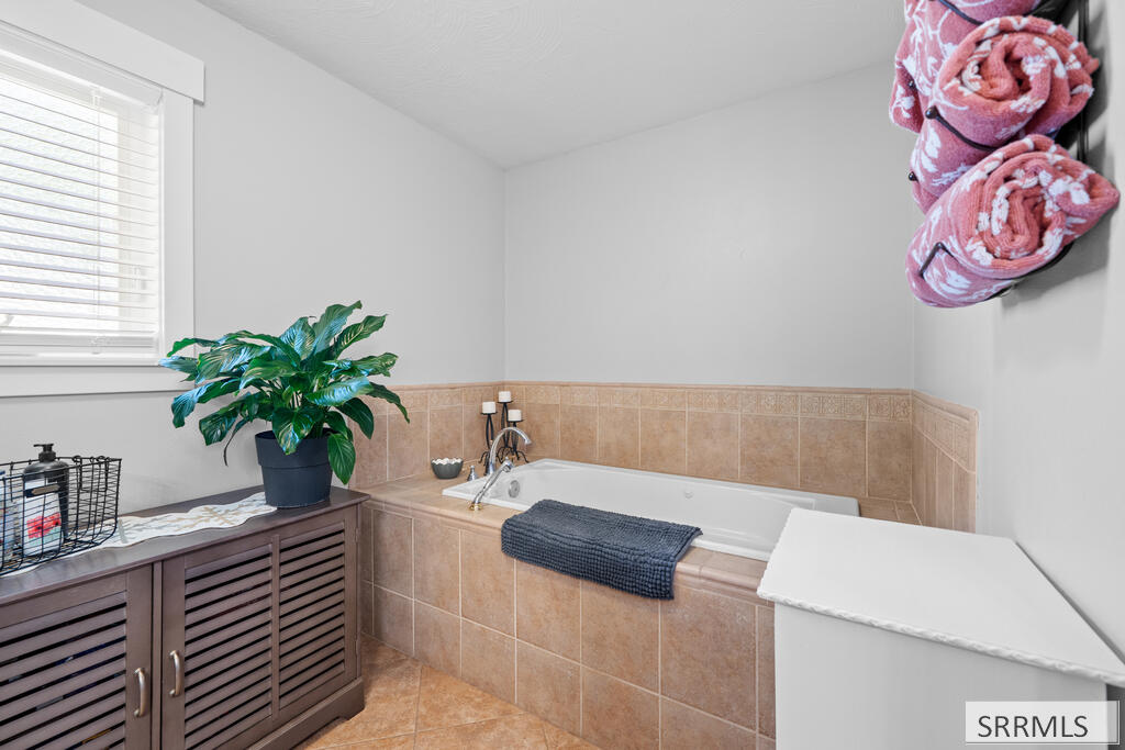 Bathroom with a tan-tiled bathtub, dark wood vanity, and pink towels hanging on the wall.