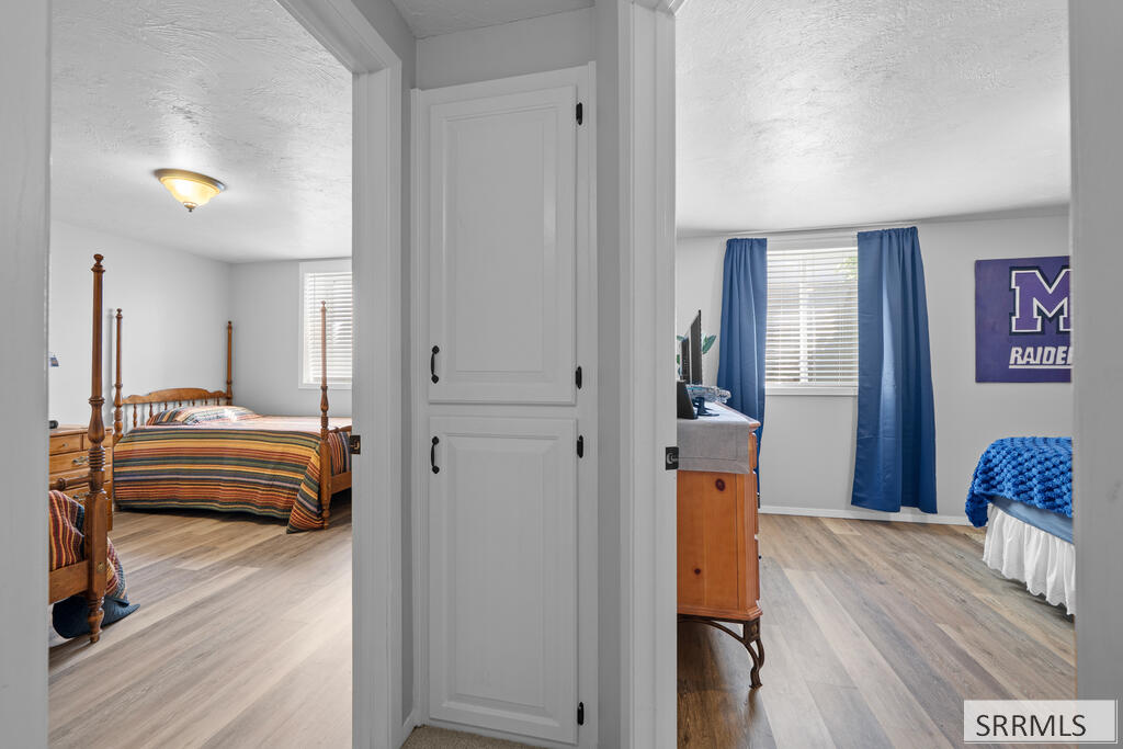 Two bedrooms viewed through a doorway, with wood-look floors and blue curtains in the right room.