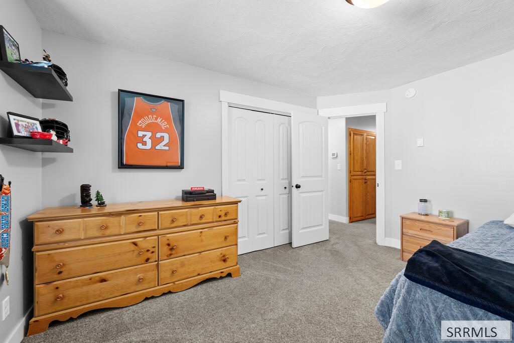 Bedroom with gray carpet, a wooden dresser, and a framed orange number 32 jersey.