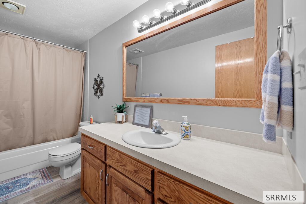 Bathroom with a long wood vanity, single sink, large mirror, and bathtub behind a beige curtain.