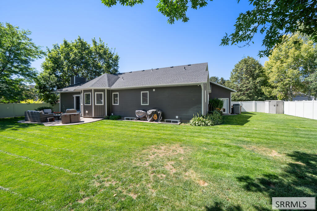 Rear of a dark gray home with a broad lawn, white fencing, and a patio seating area.