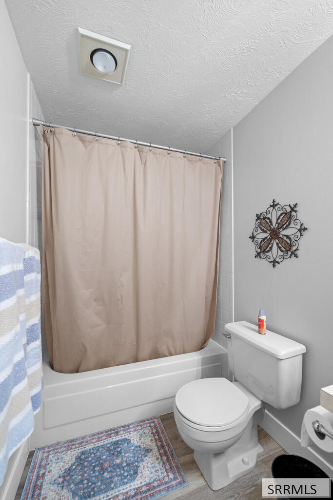 Bathroom with a beige shower curtain, white toilet, and patterned rug.