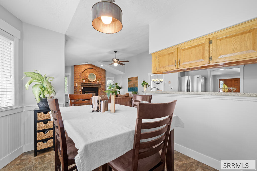 Dining area with a white-covered table, honey-colored cabinets, and a brick fireplace in the background.