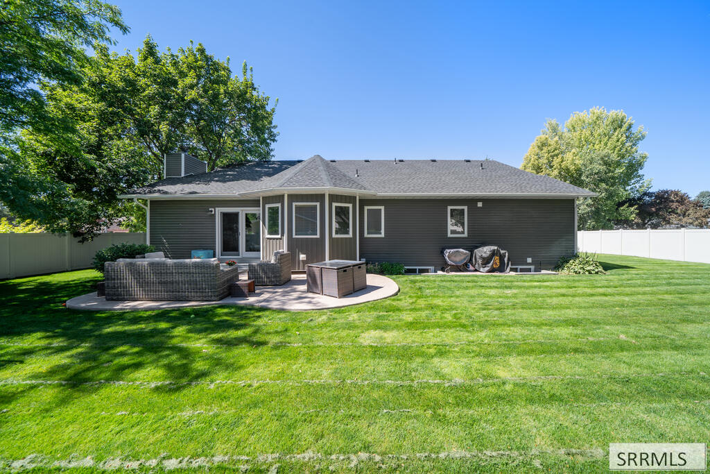 Home’s rear exterior with a broad lawn and curved patio furnished with outdoor seating.