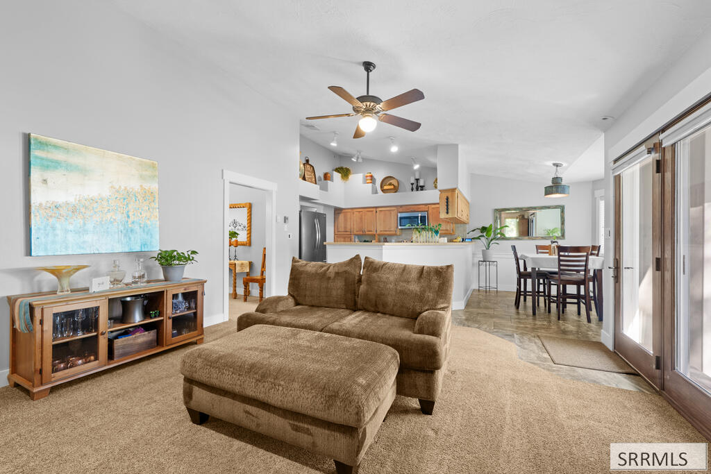 Open-plan living room with brown sofa and ottoman, kitchen, and sliding glass doors.
