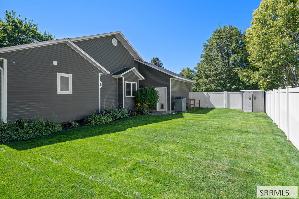 Backyard with a broad green lawn, white privacy fence, and dark gray-sided house.