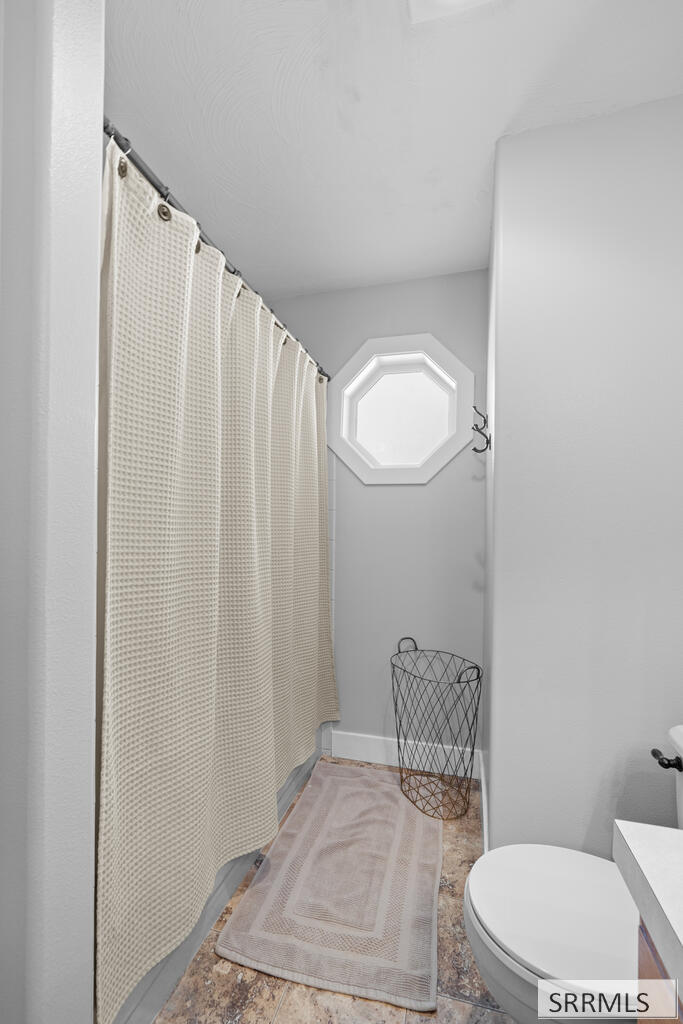 Bathroom with a cream shower curtain and octagonal window above a wire wastebasket.