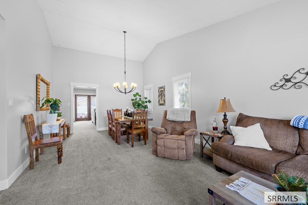 Living and dining area with gray carpet, brown seating, a wooden dining set, and a chandelier.