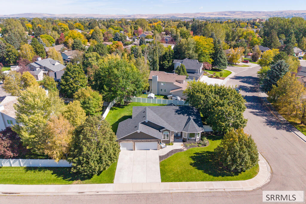 Aerial view of a gray-roofed home with a two-car garage, broad driveway, and autumn trees.